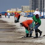 Voluntarios intentan limpiar manchas de crudo en una playa de Alabama