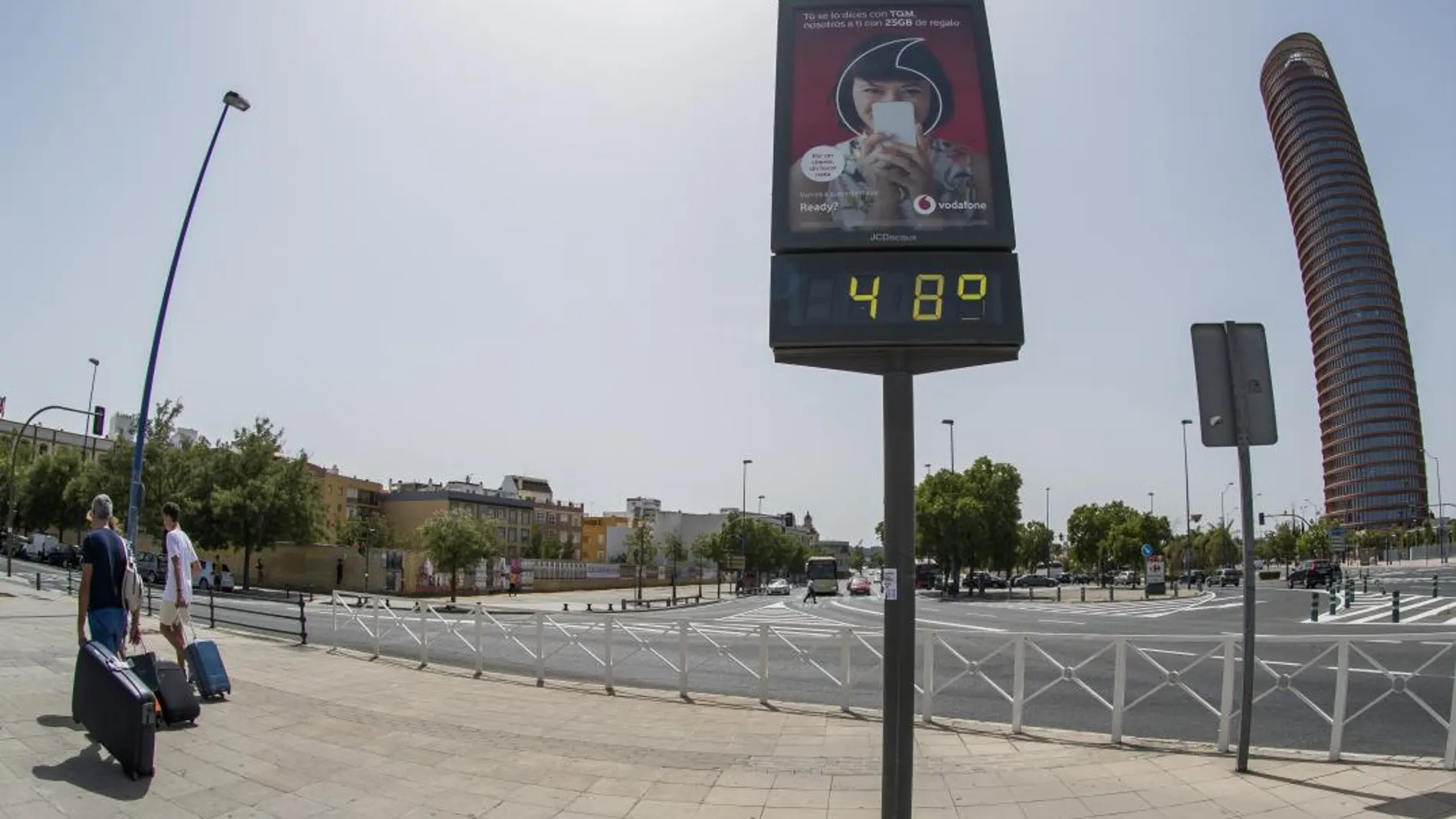 Turistas pasan junto a un termómetro de Sevilla testigo del intenso calor