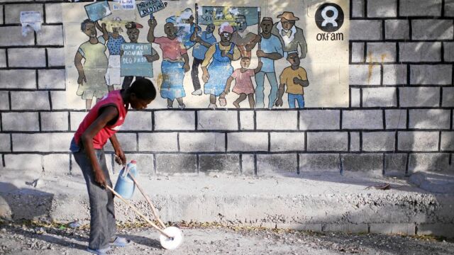 Una menor haitiana juega en una céntrica calle de Puerto Príncipe delante de un cartel de Oxfam, ONG que tapó abusos de sus trabajadores y la contratación de prostitutas en el país caribeño tras el terremoto de 2010