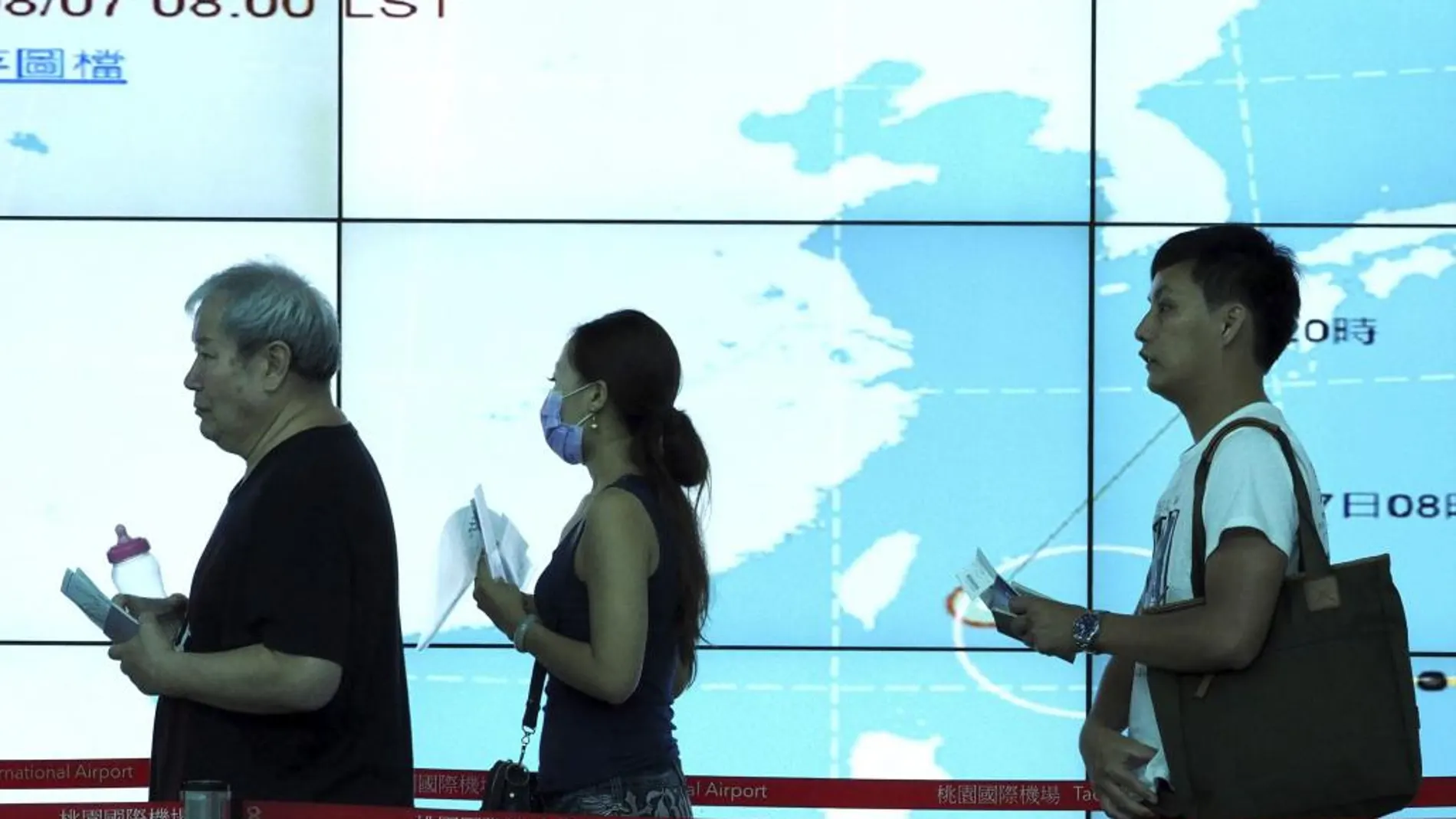 Pasajeros caminan junto a una pantalla que muestra la evolución del tifón Soudelor antes de embarcar en su vuelo en el aeropuerto Internacional de Taoyuan, taiwán.