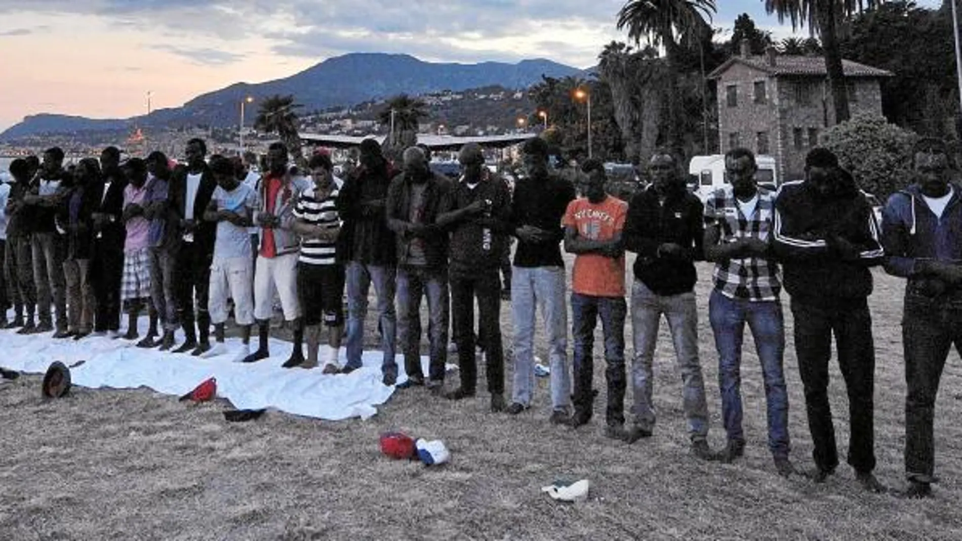 El imán Sami Bubaki dirige la oración de un grupo de inmigrantes en la playa de Ventimiglia tras la puesta de sol