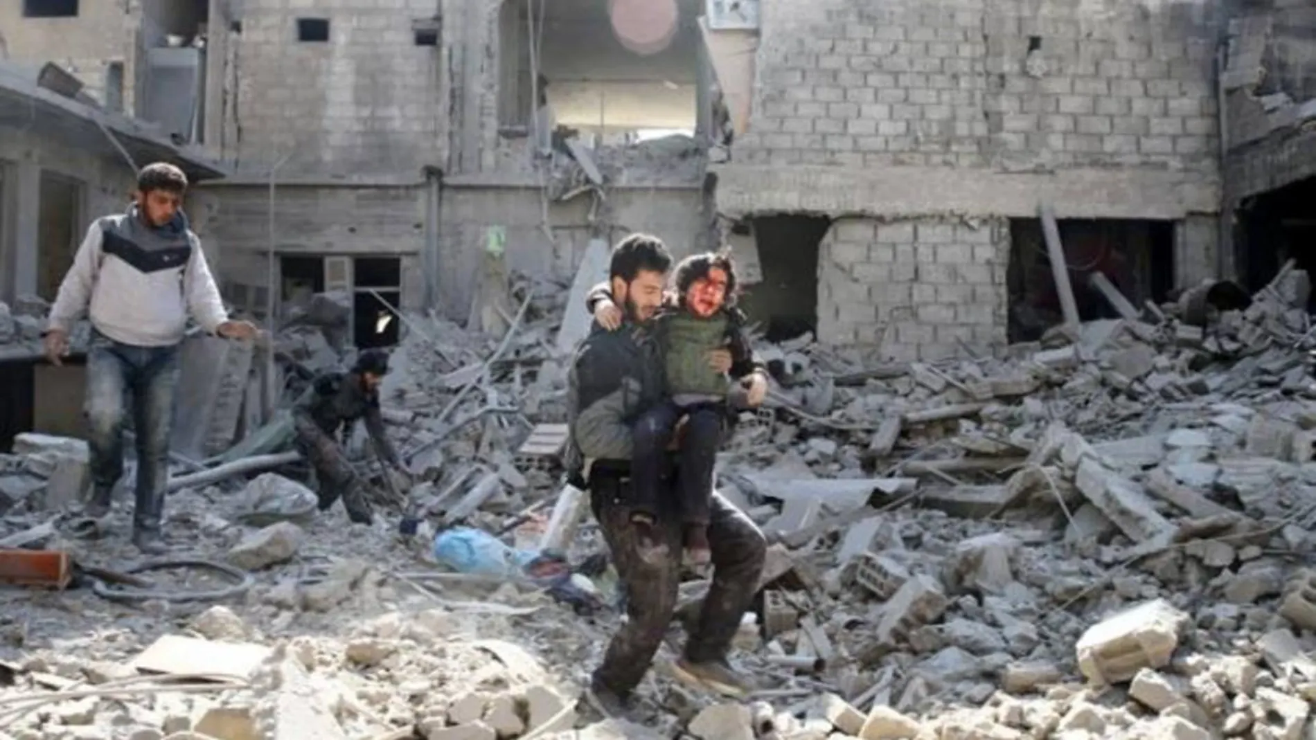 Un hombre lleva en brazos a un chico sobre los escombros de un edificio en Guta (Siria)