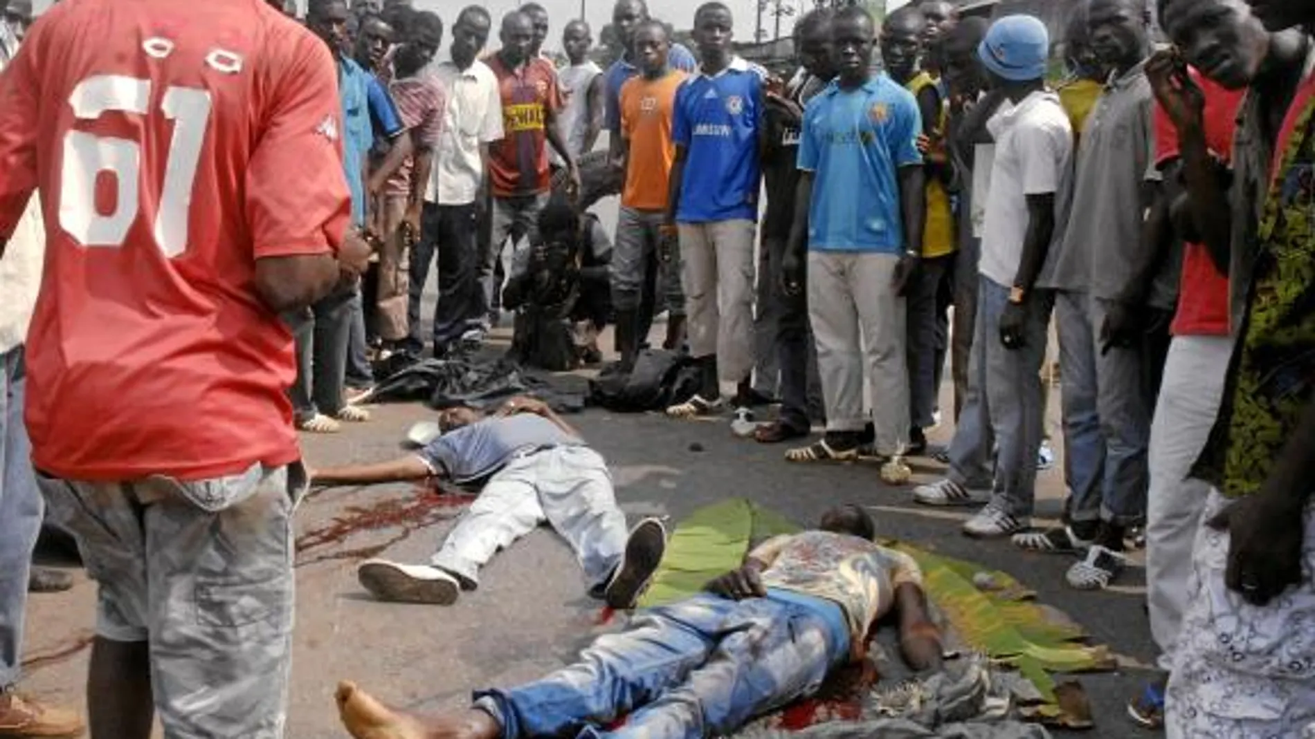 Un grupo de hombres observa los cadáveres de dos simpatizantes de Ouattara asesinados durante los recientes disturbios en Abiyán