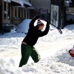 Un ciudadano trata de apartar la nieve que rodea su cohe.