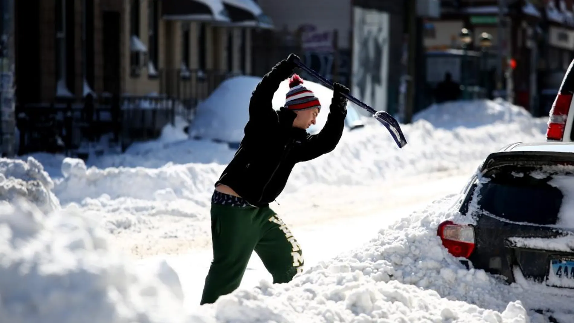 Un ciudadano trata de apartar la nieve que rodea su cohe.