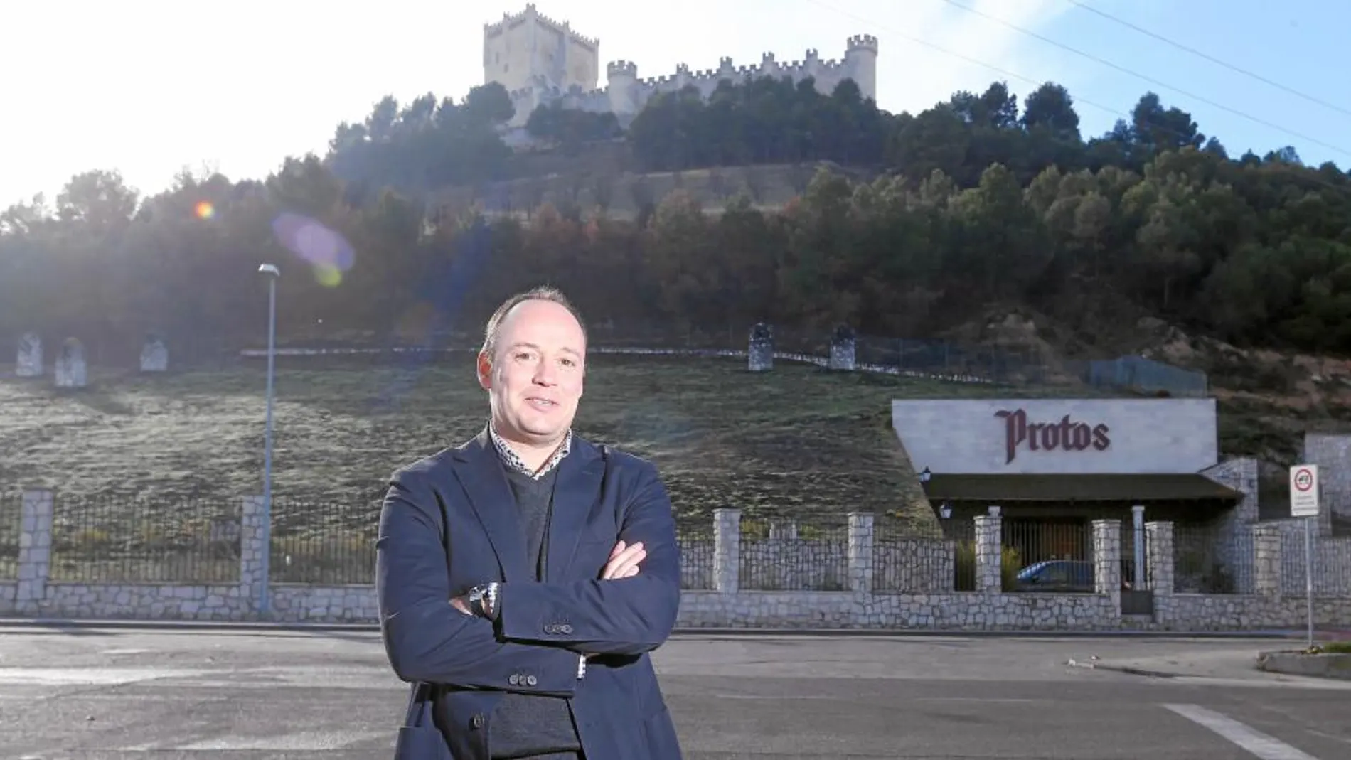 El director general de Protos, Carlos Villar, posa con las instalaciones de la bodega vieja al fondo, bajo las faldas del castillo de Peñafiel, sede del Museo Provincial del Vino de Valladolid, en lo alto, testigo de todo