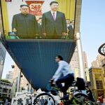 Un ciclista pasa ayer frente a una pantalla gigante emitiendo la visita de Kim Jong Un a Xi Jinping