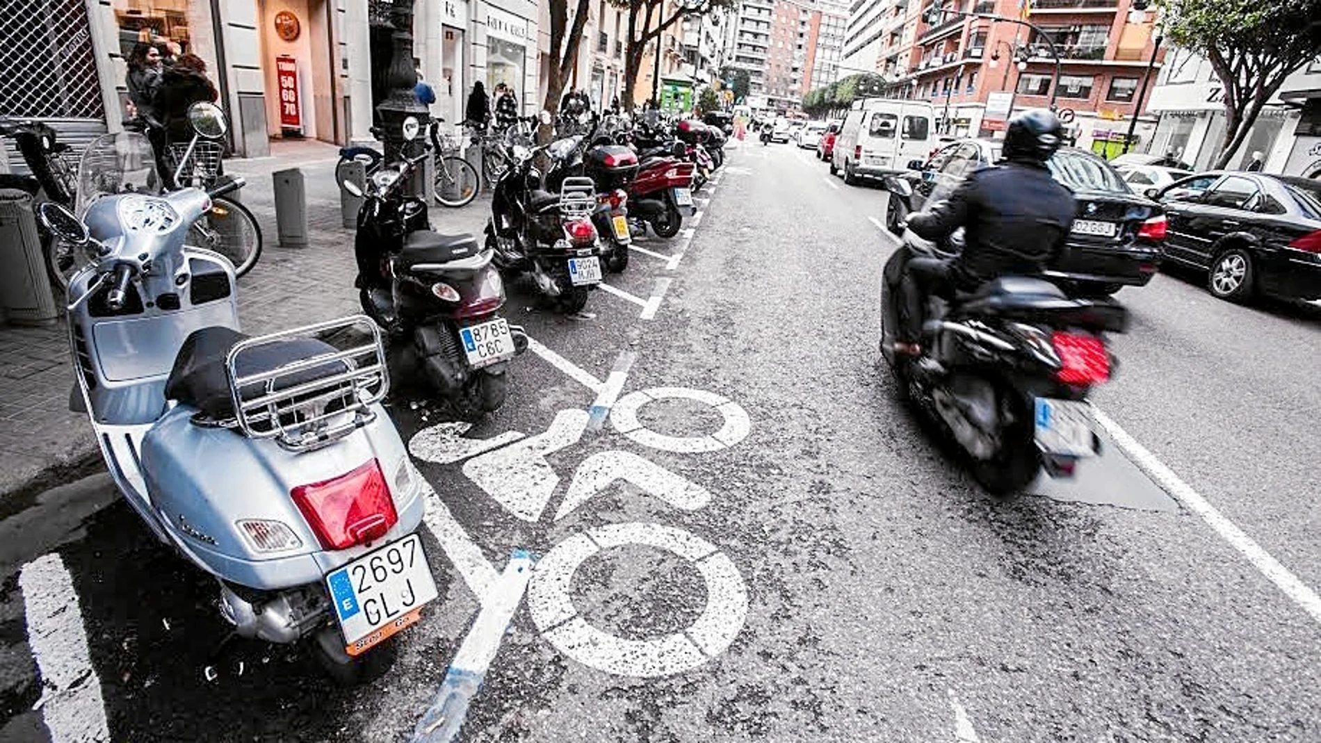 Un usuario de motocicleta circulando por la calzada y una zona de estacionamiento de motos en Valencia