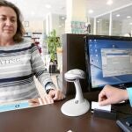 En la imagen, una dependienta entrega una tarjeta sanitaria a una clienta en una farmacia