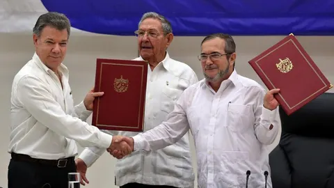El delegado de las FARC en Cuba, Rodrigo Londoño Echeverri, alias "Timochenko"(d) y el presidente de Colombia, Juan Manuel Santos (i) junto a el presidente de Cuba, Raúl Castro (c) sostienen en sus manos el acuerdo de paz entre el Gobierno colombiano y las FARC, durante la ceremonia en La Habana (Cuba)