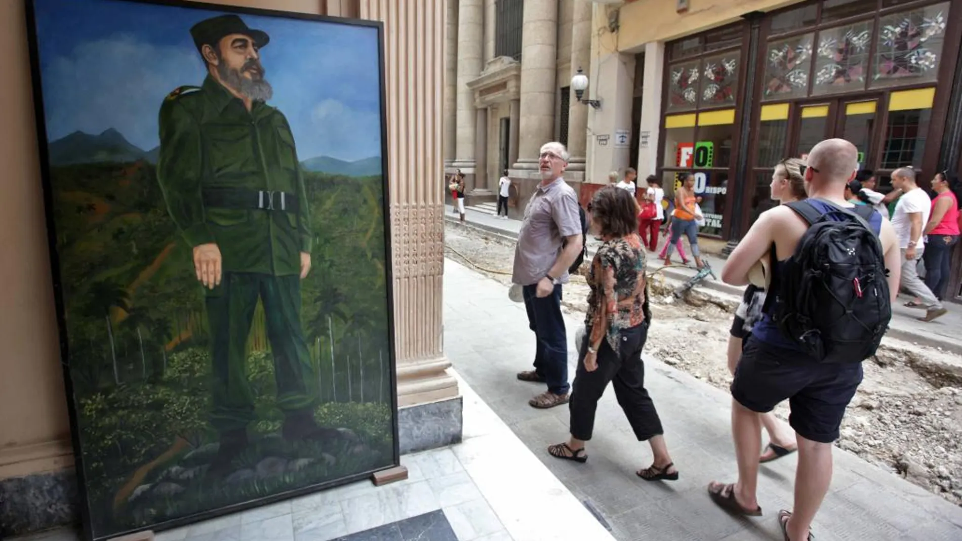Turistas caminan por un boulevard, junto a una pintura de Fidel Castro en La Habana Vieja