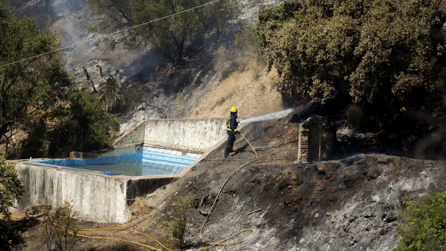 Un bombero refresca la zona durante las labores de extinción del incendio forestal declarado esta tarde en una zona cercana a la barriada de los Asperones de Málaga capital
