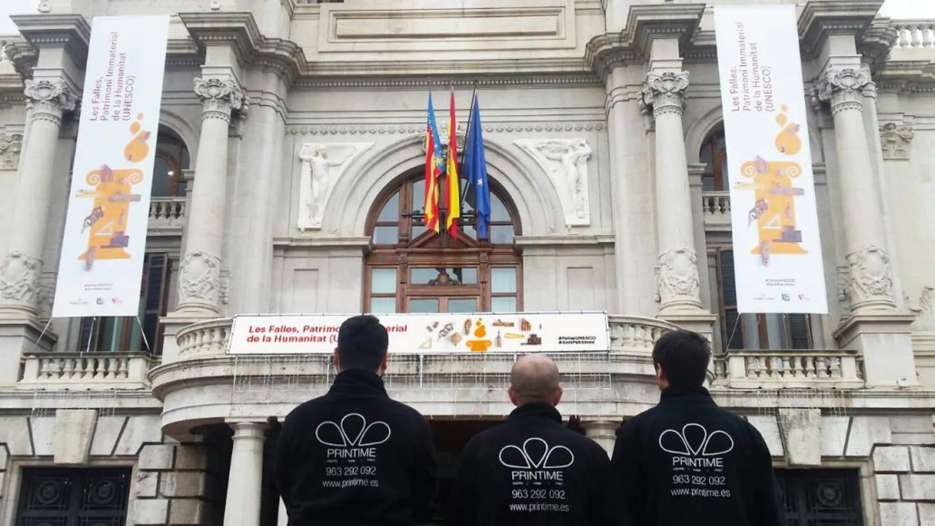 Un grupo de trabajadores de PrinTime observa los estandartes colocados en la fachada del Ayuntamiento.