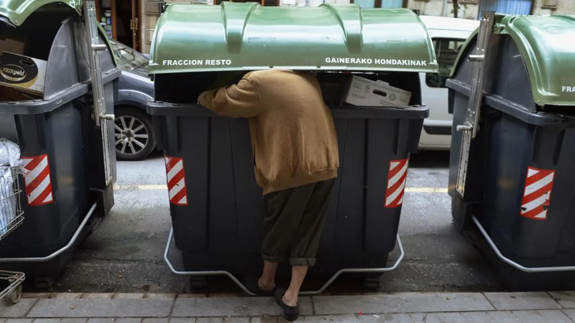 Una mujer rebusca en un contenedor de basura en una calle de Bilbao