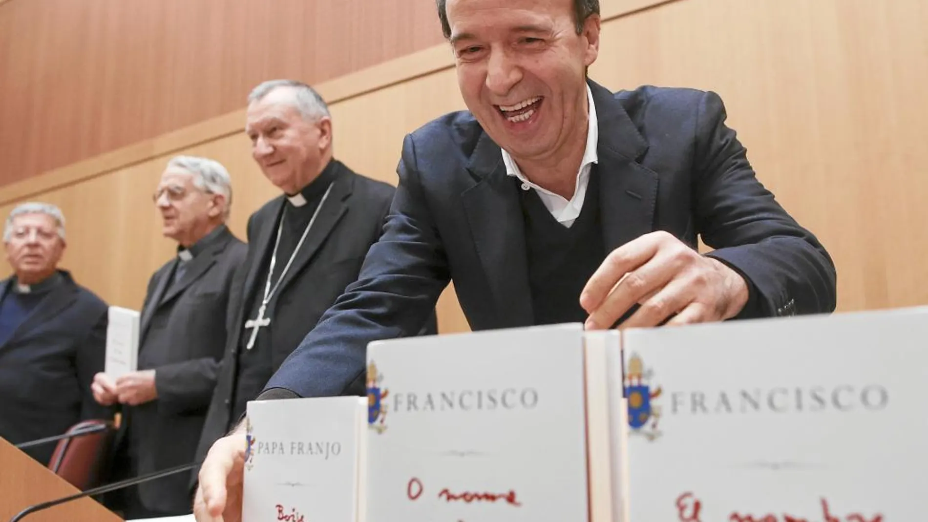 En primer plano, el cómico Roberto Benigni coloca varias ediciones del libro del Papa. Detrás, Pietro Parolin y Federico Lombardi