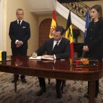 El rey Felipe, en presencia de la reina Letizia y del embajador de Bélgica en España, Pierre Labouverie (i), firma en el libro de condolencias en la residencia del embajador.