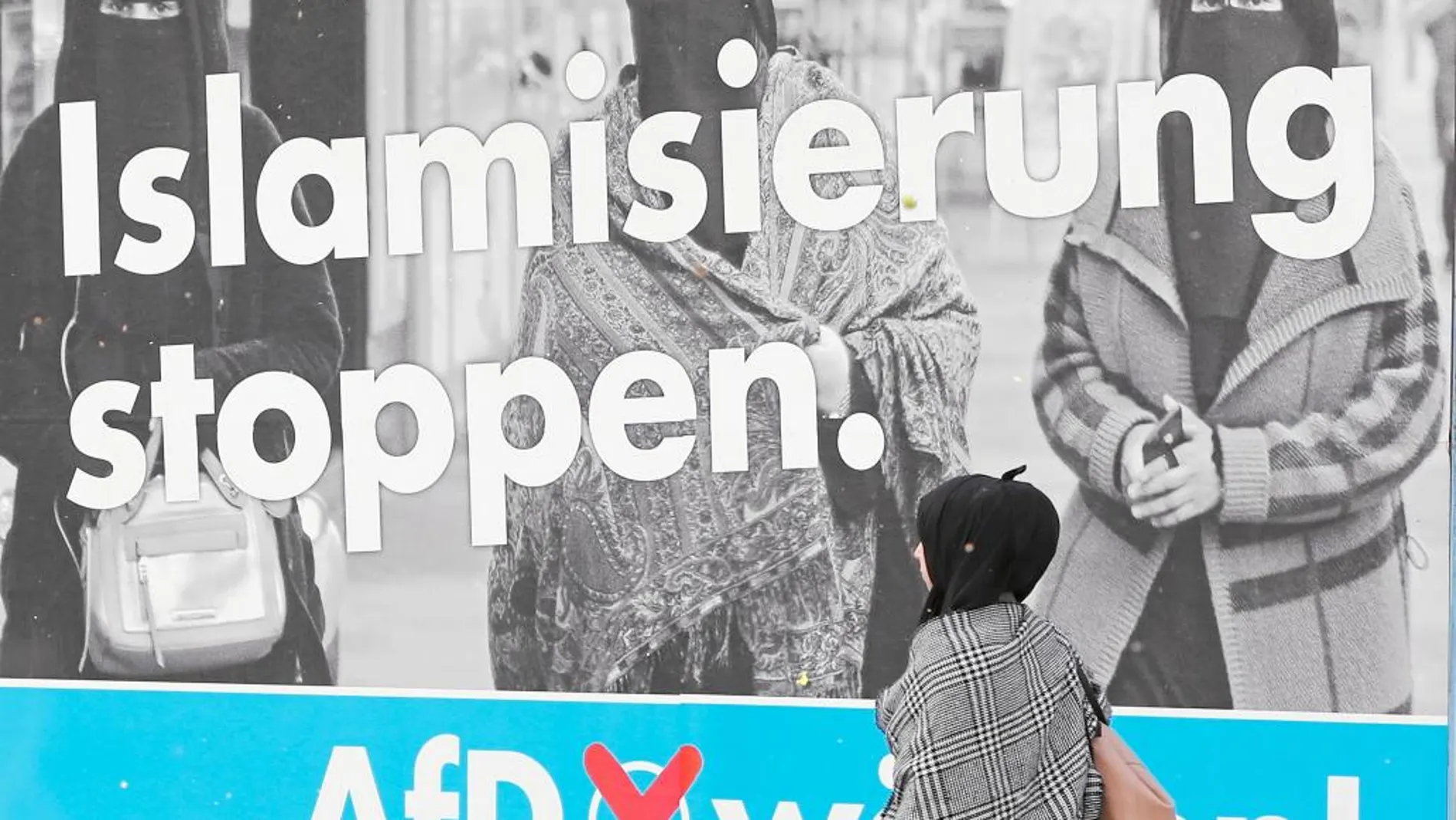 Una mujer musulmana camina ante un cartel antiinmigración del partido ultraderechista Alternativa para Alemania