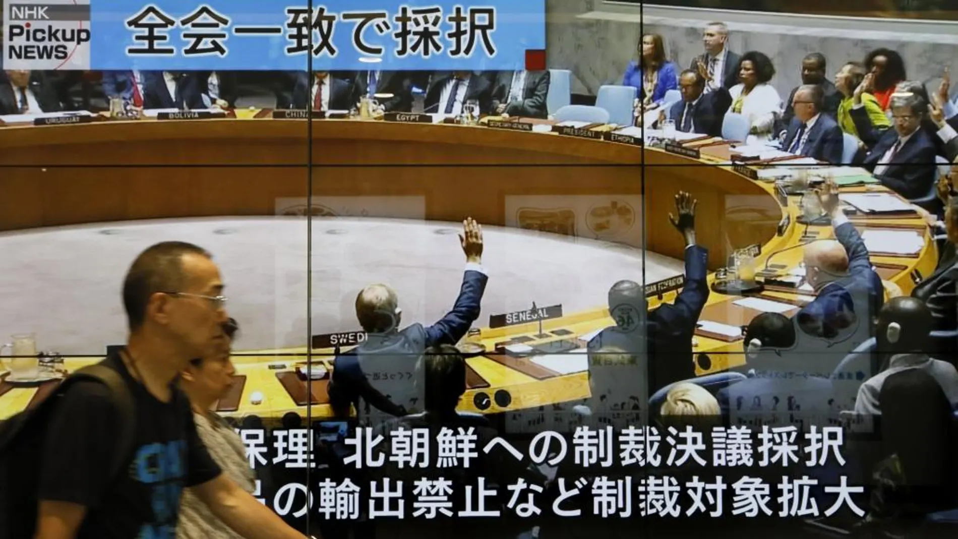 Peatones caminan frente a una enorme pantalla que muestra un programa de noticias de televisión que informa sobre la sesión del Consejo de Seguridad de la ONU en Nueva York que acordó sanciones contra Corea del Norte hoy, en Tokio (Japón)