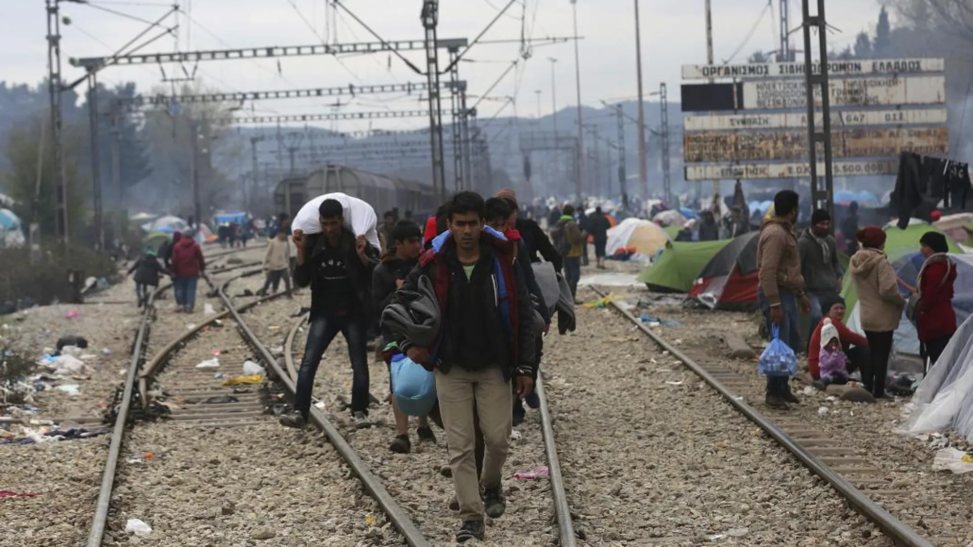 Un grupo de refugiados camina por las vías del tren en el campamento provisional de refugiados en Idomeni