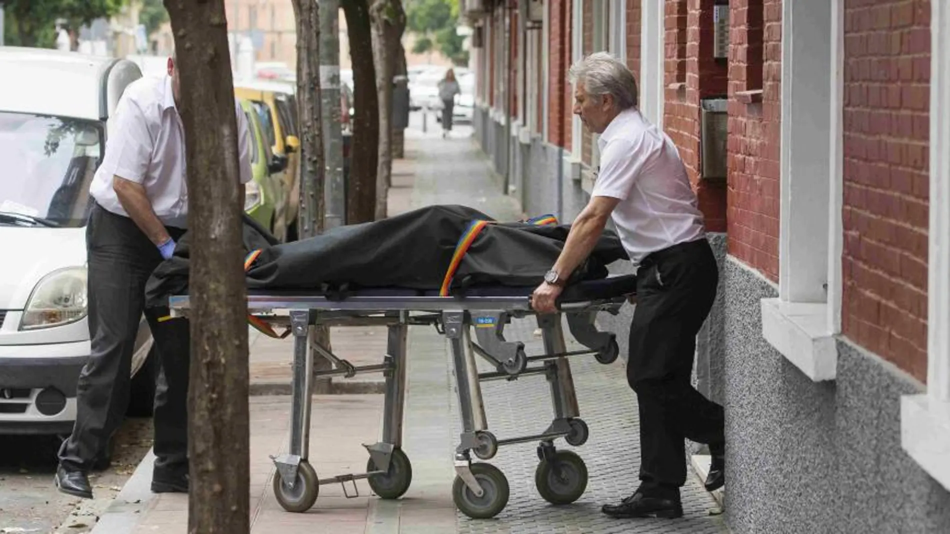 Operarios de la funeraria trasladan el cadáver de una mujer, de 55 años que ha sido hallado hoy en una vivienda en Sevilla con un arma blanca en el pecho.