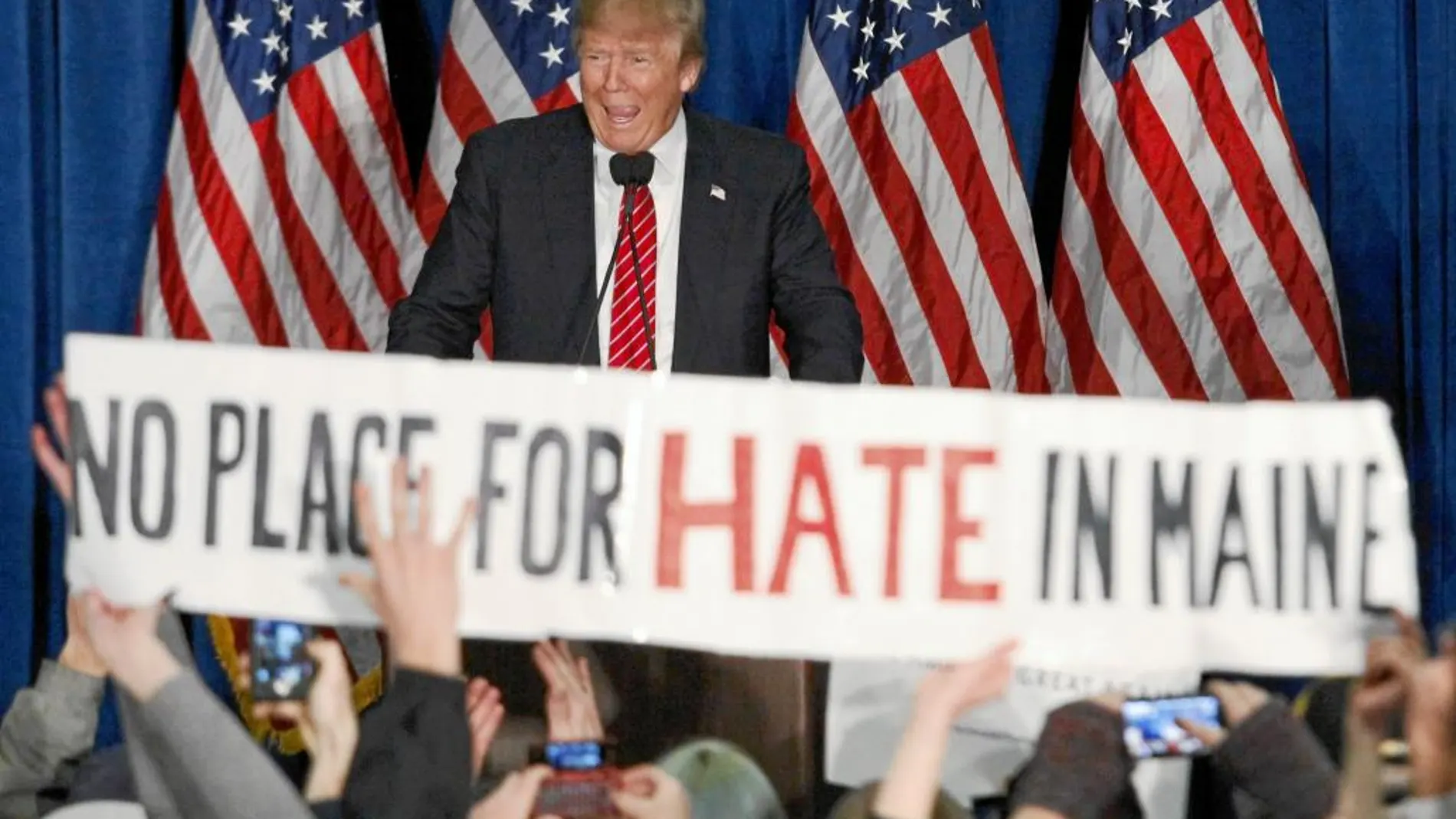 Donald Trump sonríe a un grupo de seguidores con un cartel en el que se lee: «No hay sitio para el odio en Maine»
