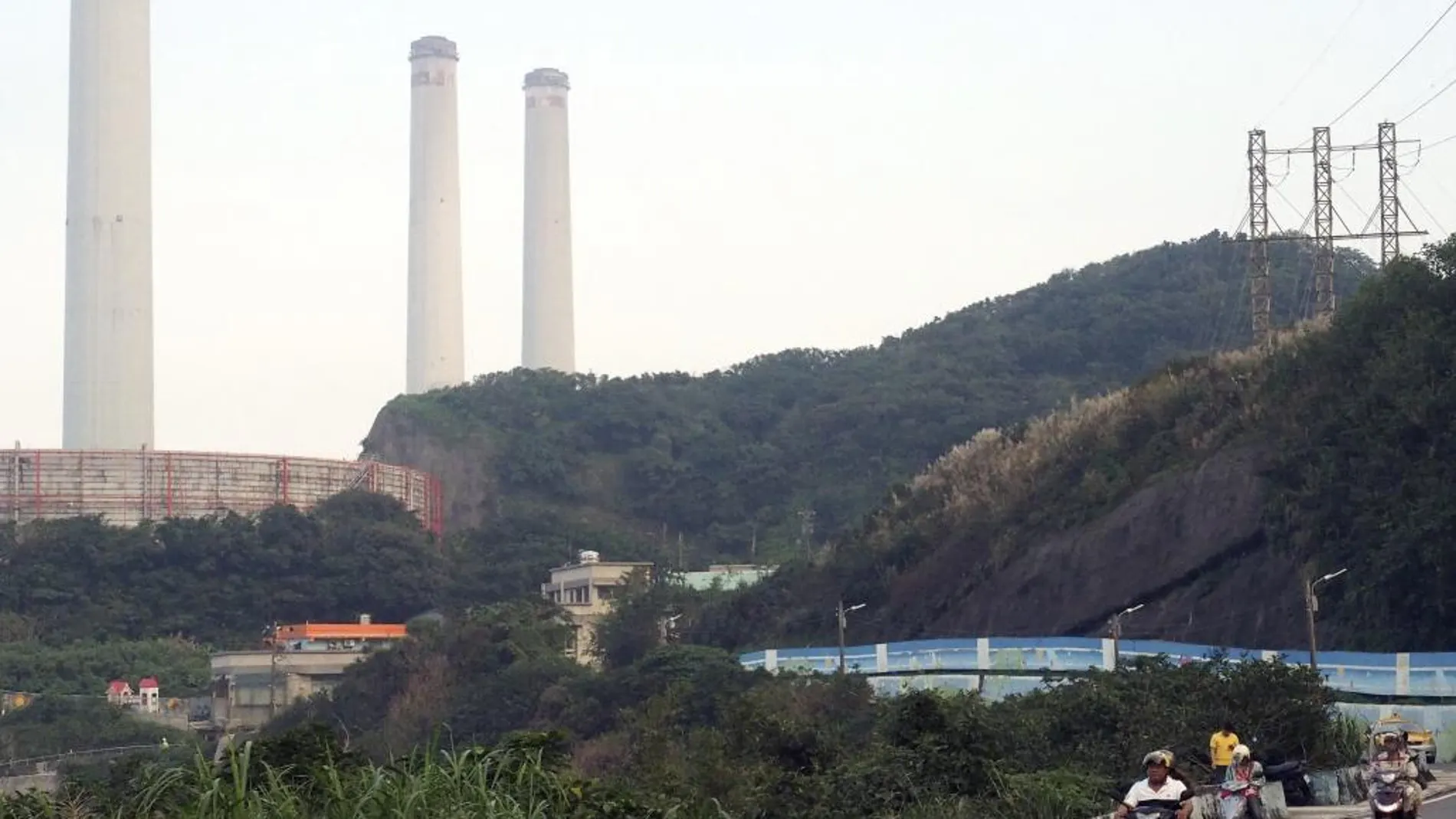 Un grupo de motocicletas pasa junto a las chimeneas de la central eléctrica de Hsieh-ho en Keelung, Taiwán