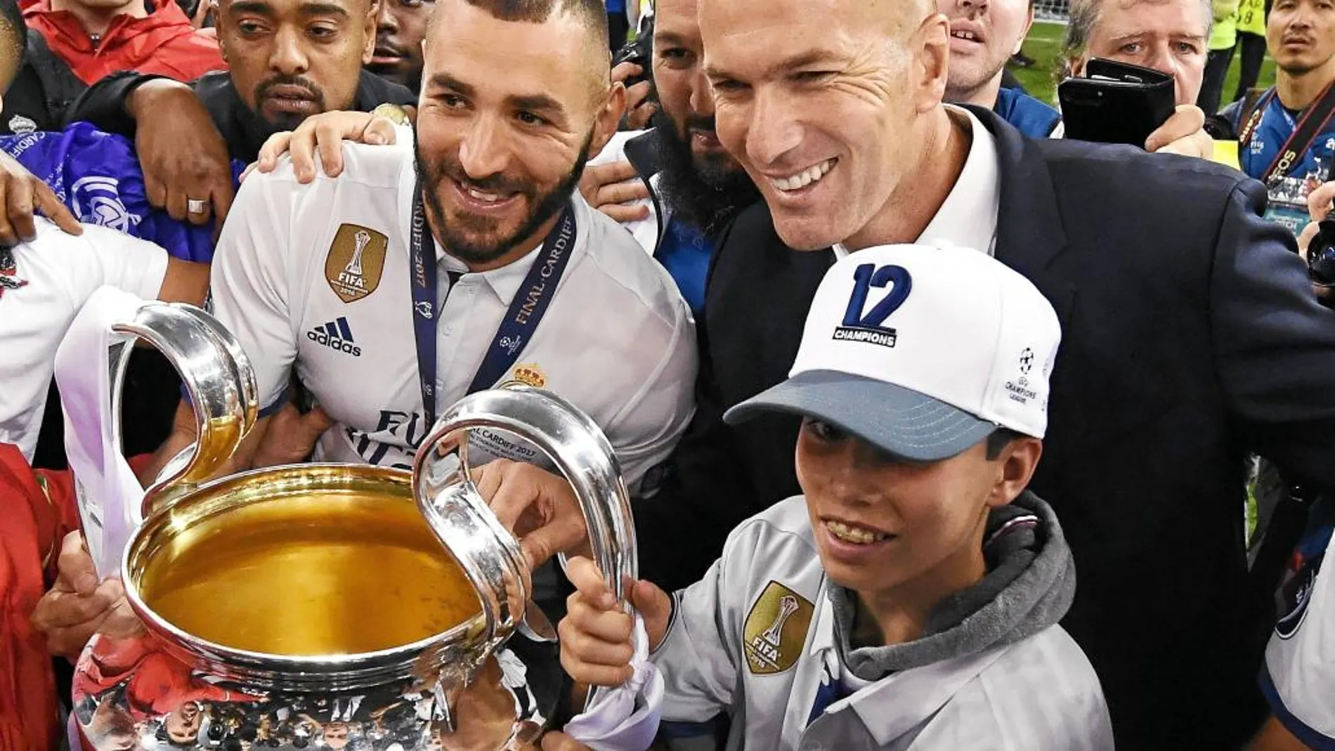 Benzema y Zidane. se hacen una foto con el trofeo de la Champions sobre el césped del Millenium de Cardiff