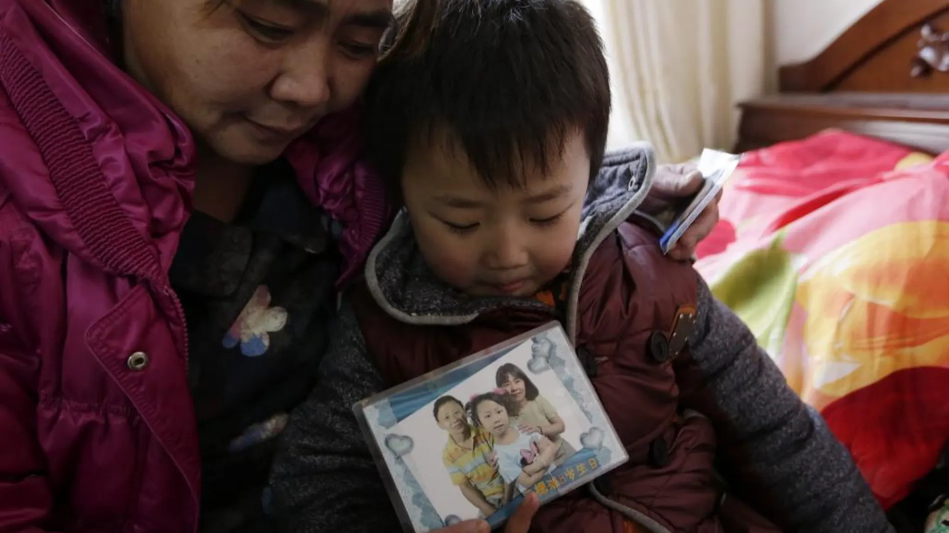 Mei Qiuyu (izda) y su hijo Wang Zhongsheng (dcha) muestran una fotografía de su otra hija y su marido en su casa en el distrito de Daxing en Pekín