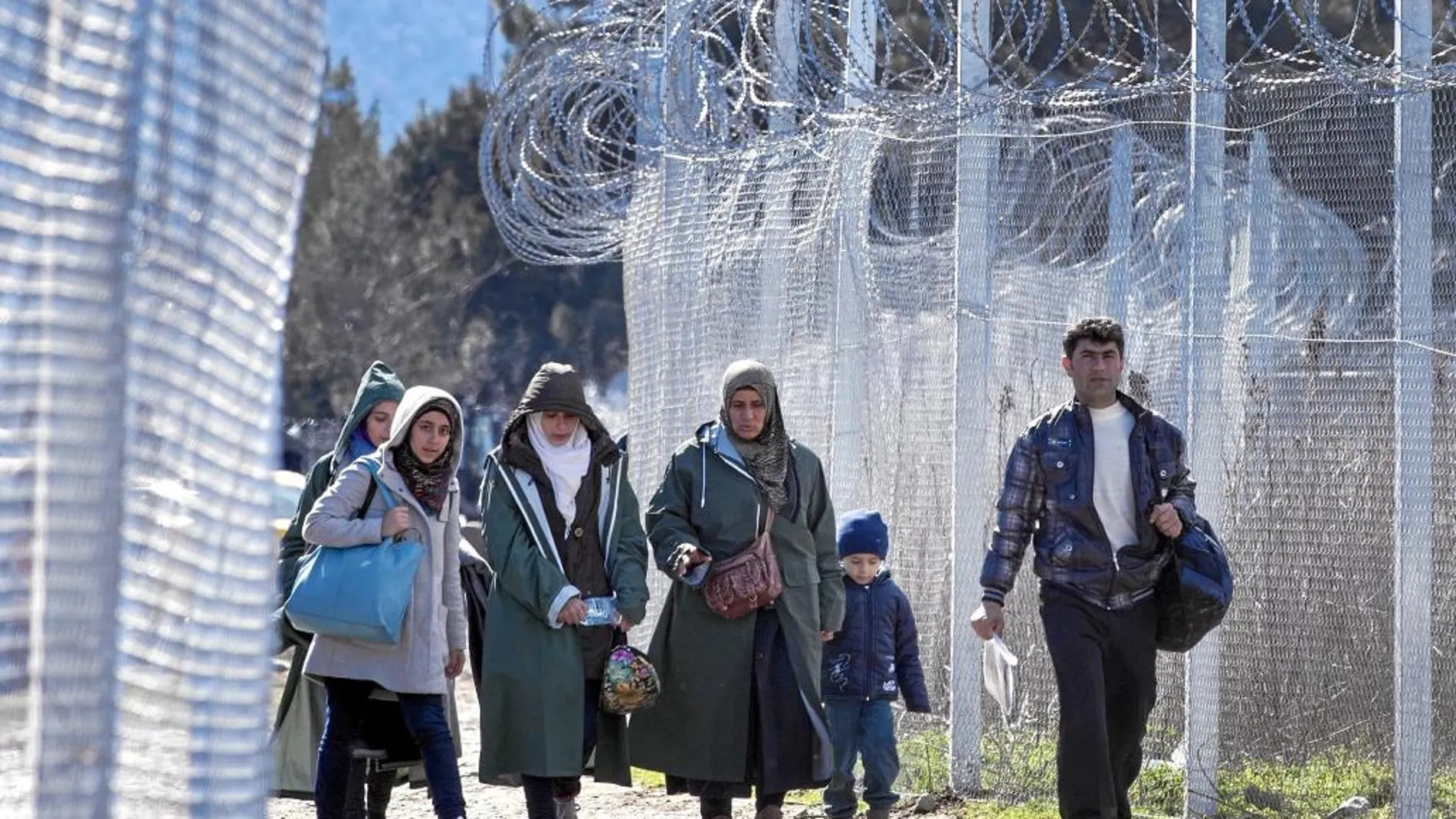 Varios inmigrantes caminan junto a las vallas entre Macedonia y Grecia tras cruzar la frontera cerca de Gevgelija