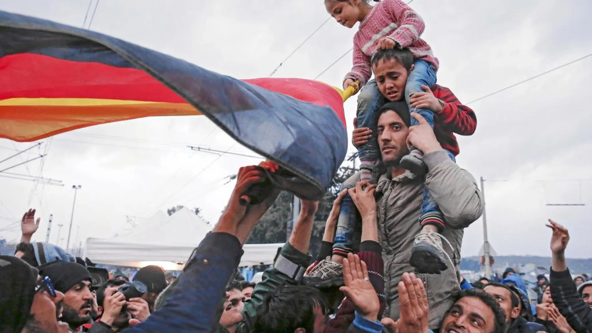 Un grupo de refugiados ondea una bandera alemana en la frontera entre Grecia y Macedonia, cerca de Idomeni