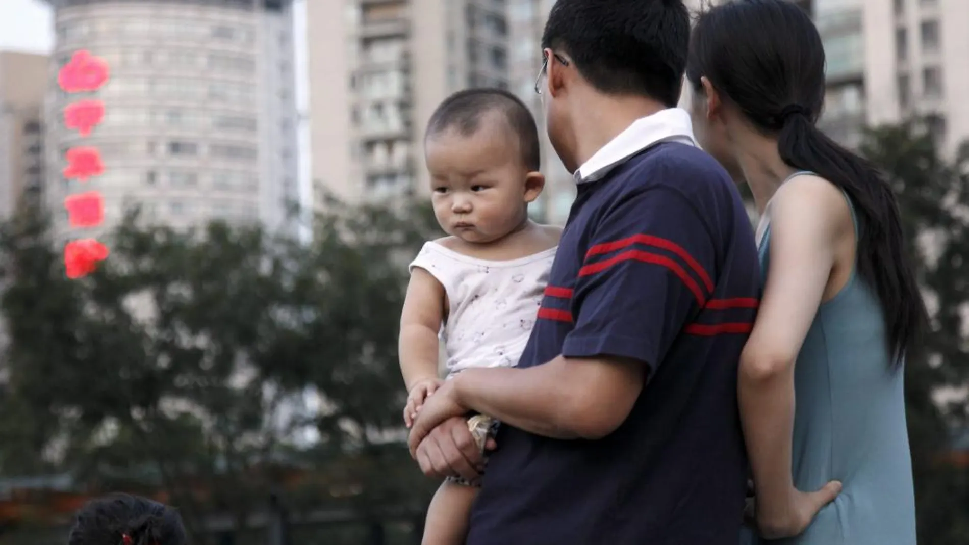 Una pareja observa a unos niños jugando en un parque cargando a su bebé en Shangai (China)