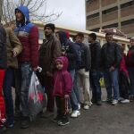 Migrantes y refugiados hacen cola para recibir alimentos repartidos por voluntarios en el puerto del Pireo (Grecia)