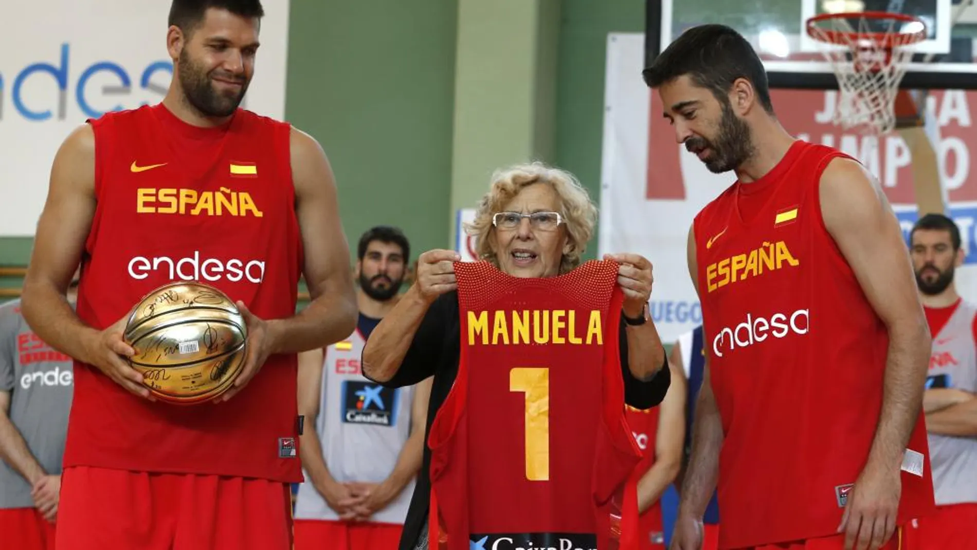 La alcaldesa de Madrid, Manuela Carmena, recibe de manos de los jugadores Felipe Reyes y Juan Carlos Navarro (d), una camiseta del equipo con su nombre tras asistir al entrenamiento de la selección española de baloncesto.