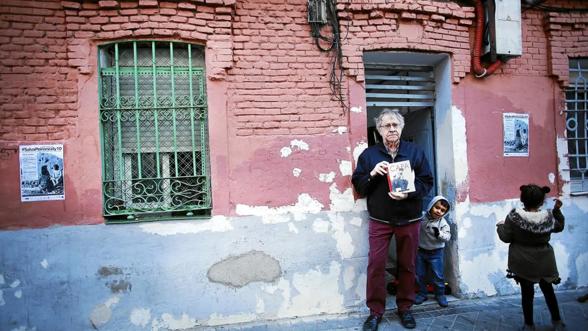 El historiador Ian Gibson, ayer, ante la famosa fachada que fotografió Robert Capa, con un libro del fotógrafo