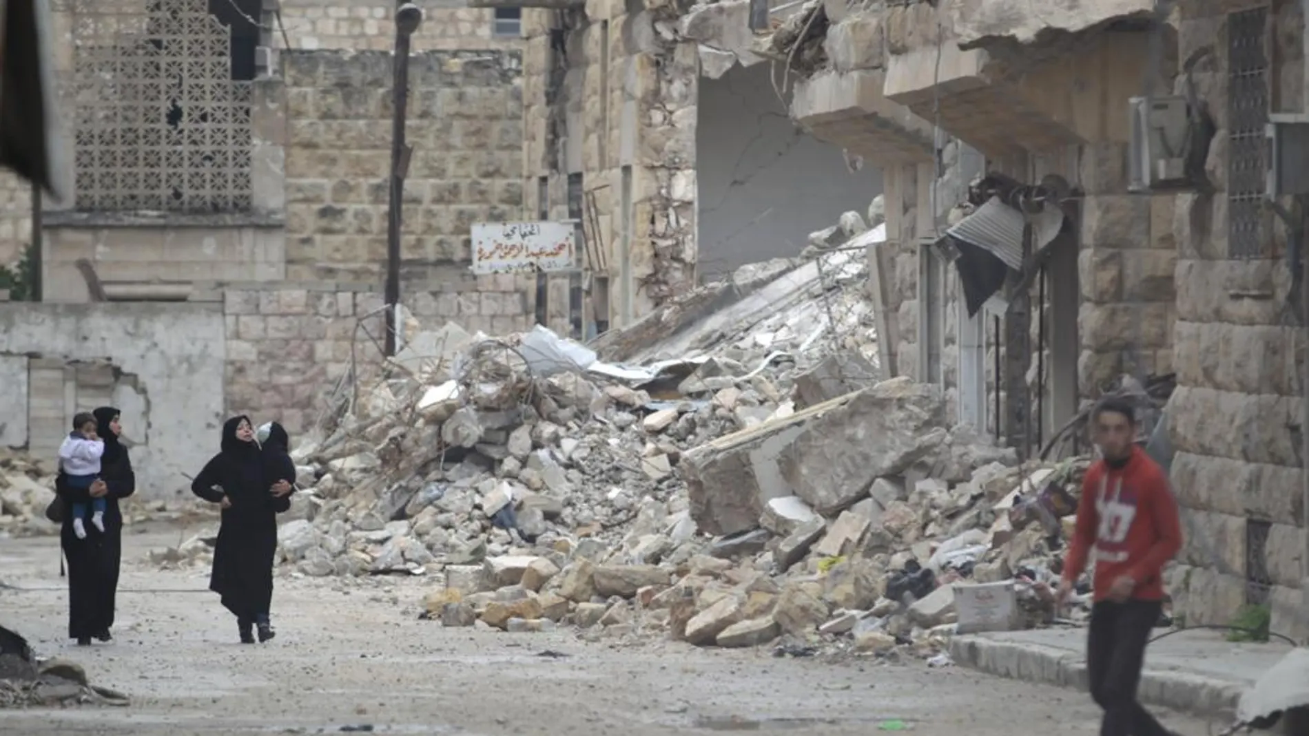 Varios civiles pasan por una calle con edificios en ruinas por los bombardeos en la zona de Maaret al-Numan, controlada por los rebeldes