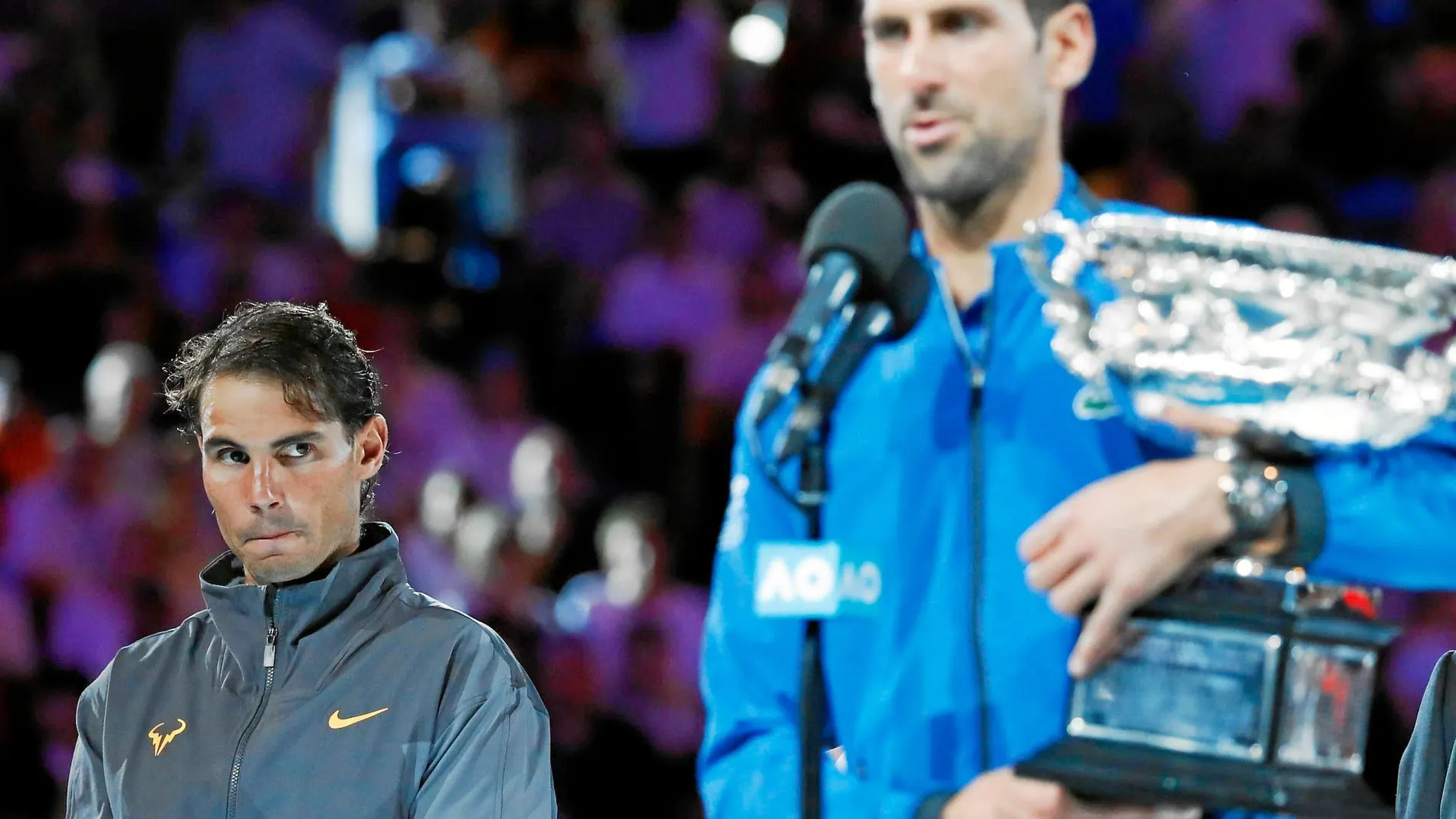 Nadal mira cómo Novak Djokovic sostiene su séptimo título en Australia y se dirige al público de la Rod Laver Arena durante la entrega de trofeos