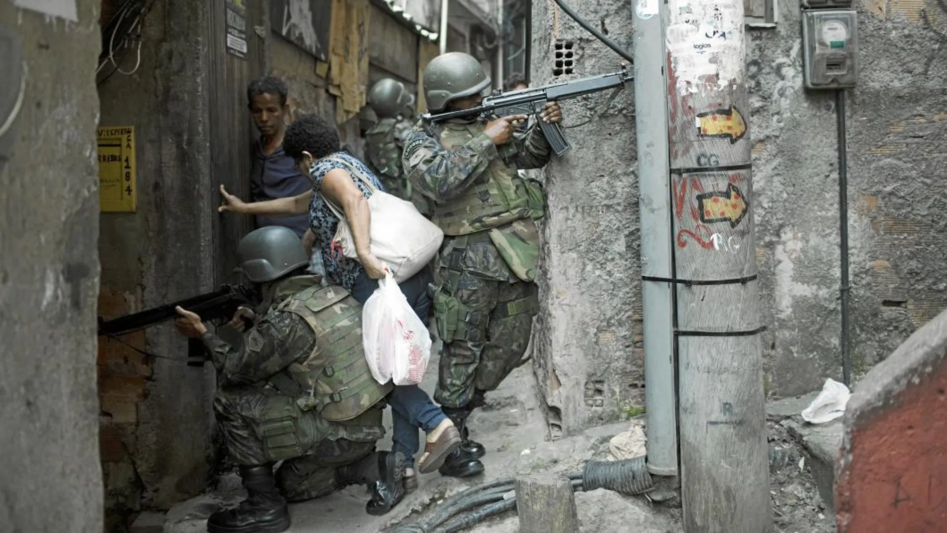 Una mujer cruza entre soldados mientras patrullan en un callejón durante una operación en la favela de Rocinha, en Río de Janeiro