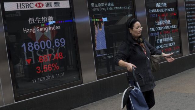 Una mujer camina junto a unas pantallas informativas que muestran la información bursátil en Hong Kong (China) el 11 de febrero de 2016