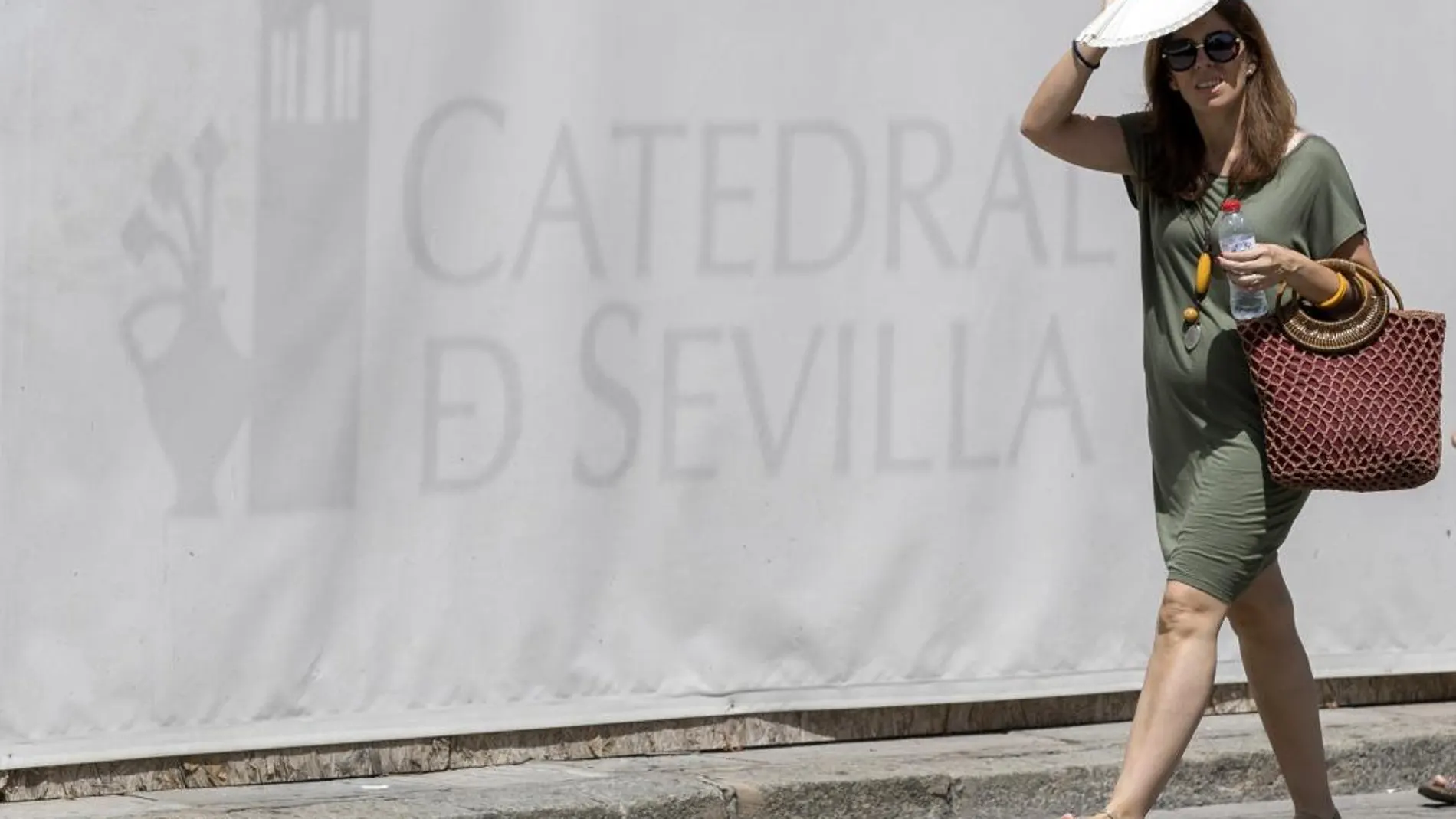 Una turista pasa junto a la Catedral de Sevilla protegiéndose del sol con un abanico