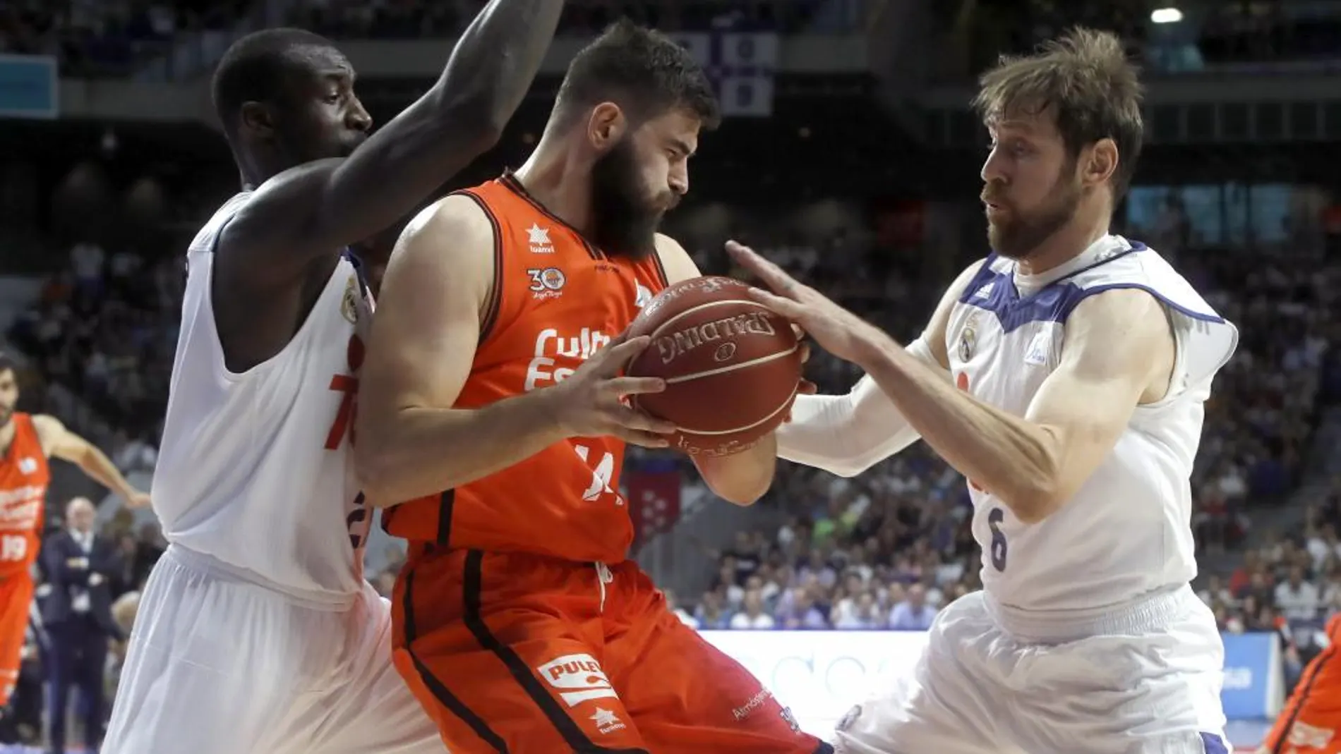 Los jugadores del Real Madrid Andrés Nocioni (d) y Othello hunter (i) intentan arrebatar el balón al pívot del Valencia Basket Bojan Dubljevic