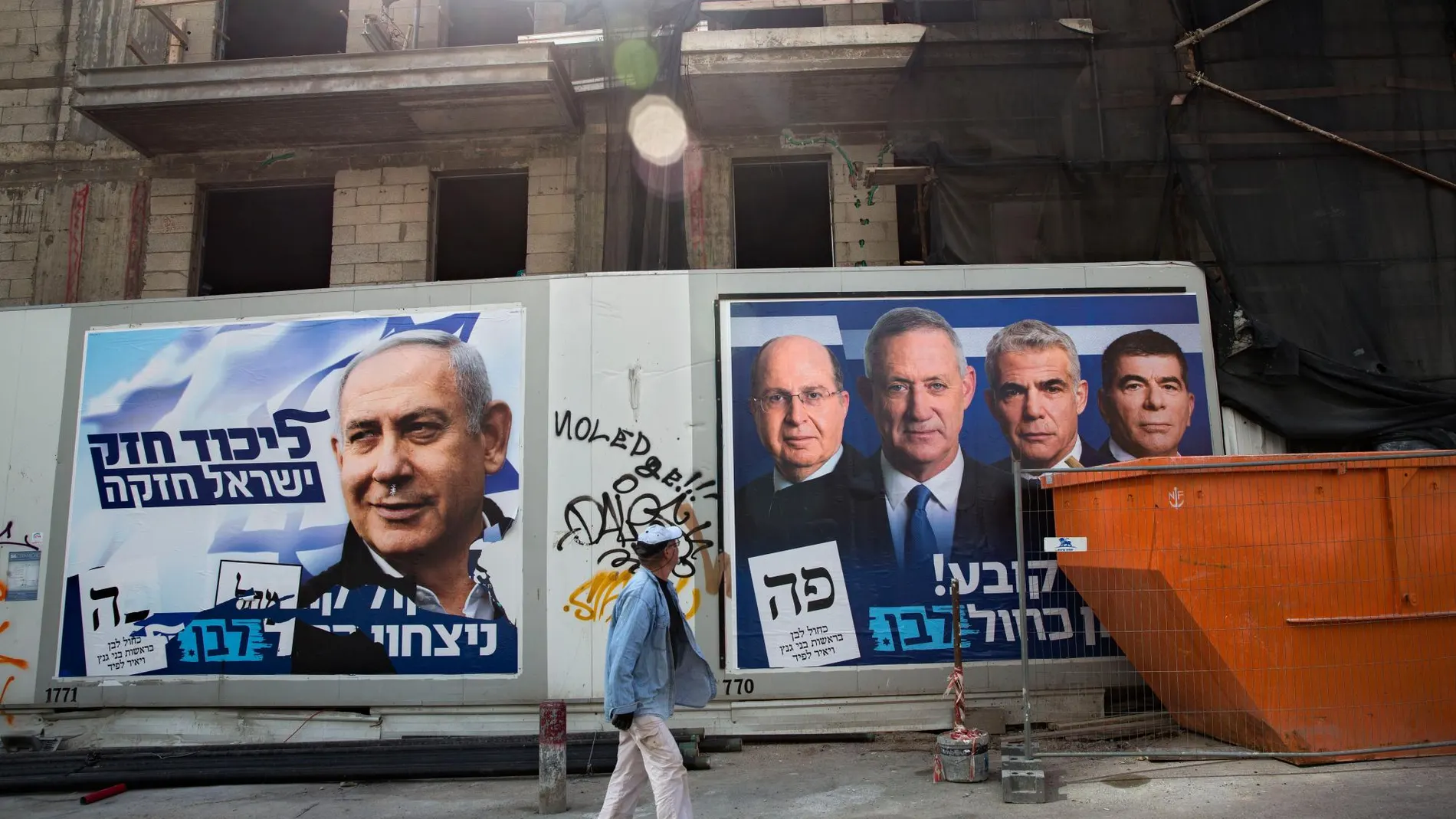 Un hombre camina por una calle junto a carteles electorales con los principales candidatos