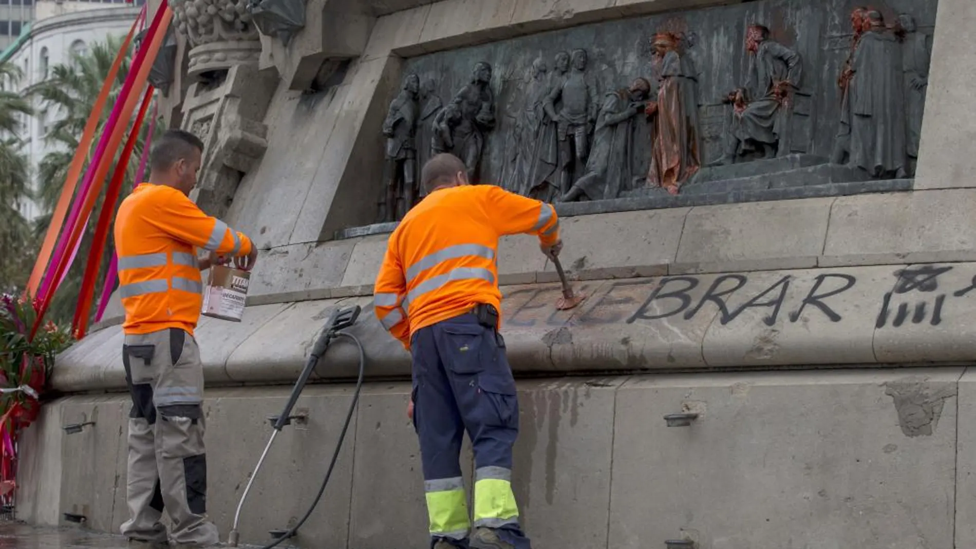 Operarios del servicio de limpieza del Ayuntamiento de Barcelona limpian las pintadas que han aparecido en el monumento a Cristóbal Colón