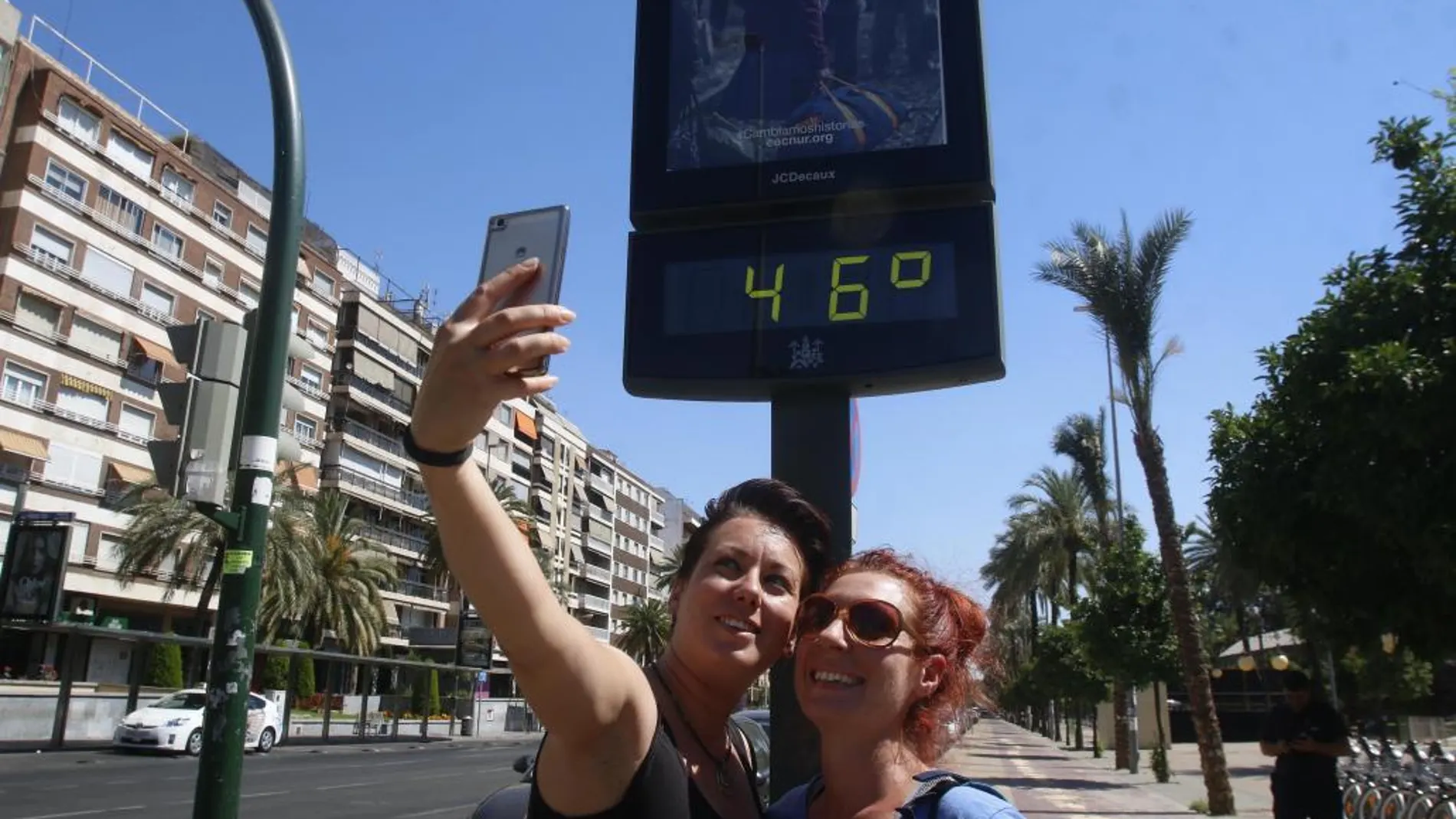 Dos jóvenes se hacen un selfi con el panel del termómetro de la calle que registra 46 grados en una zona del centro de Córdoba