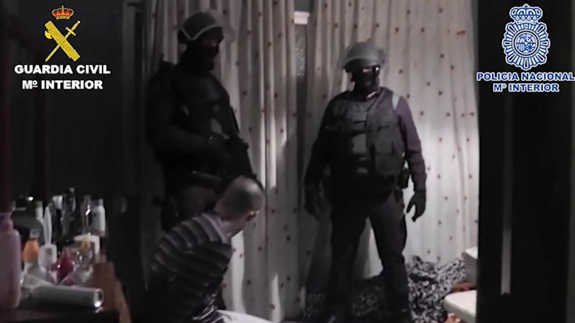 Dos agentes participantes en el operativo custodian a uno de los detenidos