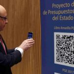 Cristóbal Montoro, escanea con el móvl el código QR del proyecto de Ley de Presupuestos Generales del Estado (PGE) para 2017, poco antes de la rueda de prensa que ha ofrecido hoy en el Congreso para presentarlo.