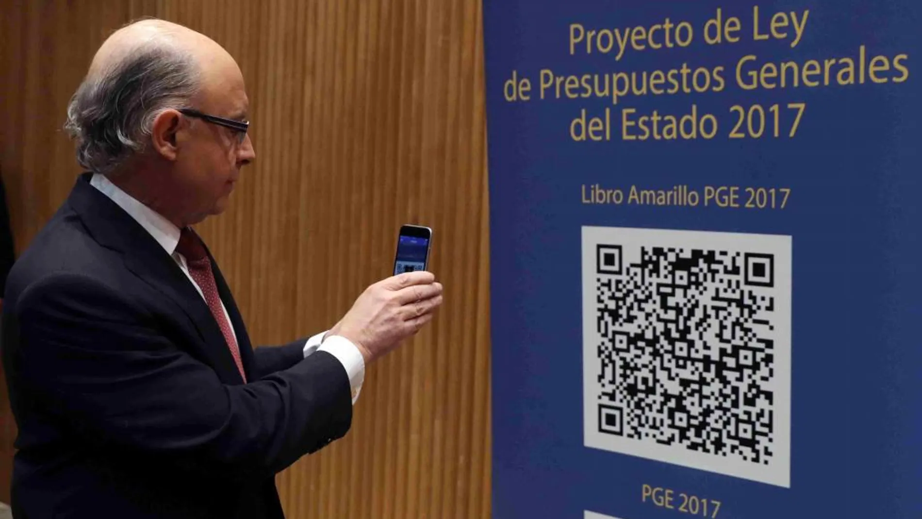 Cristóbal Montoro, escanea con el móvl el código QR del proyecto de Ley de Presupuestos Generales del Estado (PGE) para 2017, poco antes de la rueda de prensa que ha ofrecido hoy en el Congreso para presentarlo.