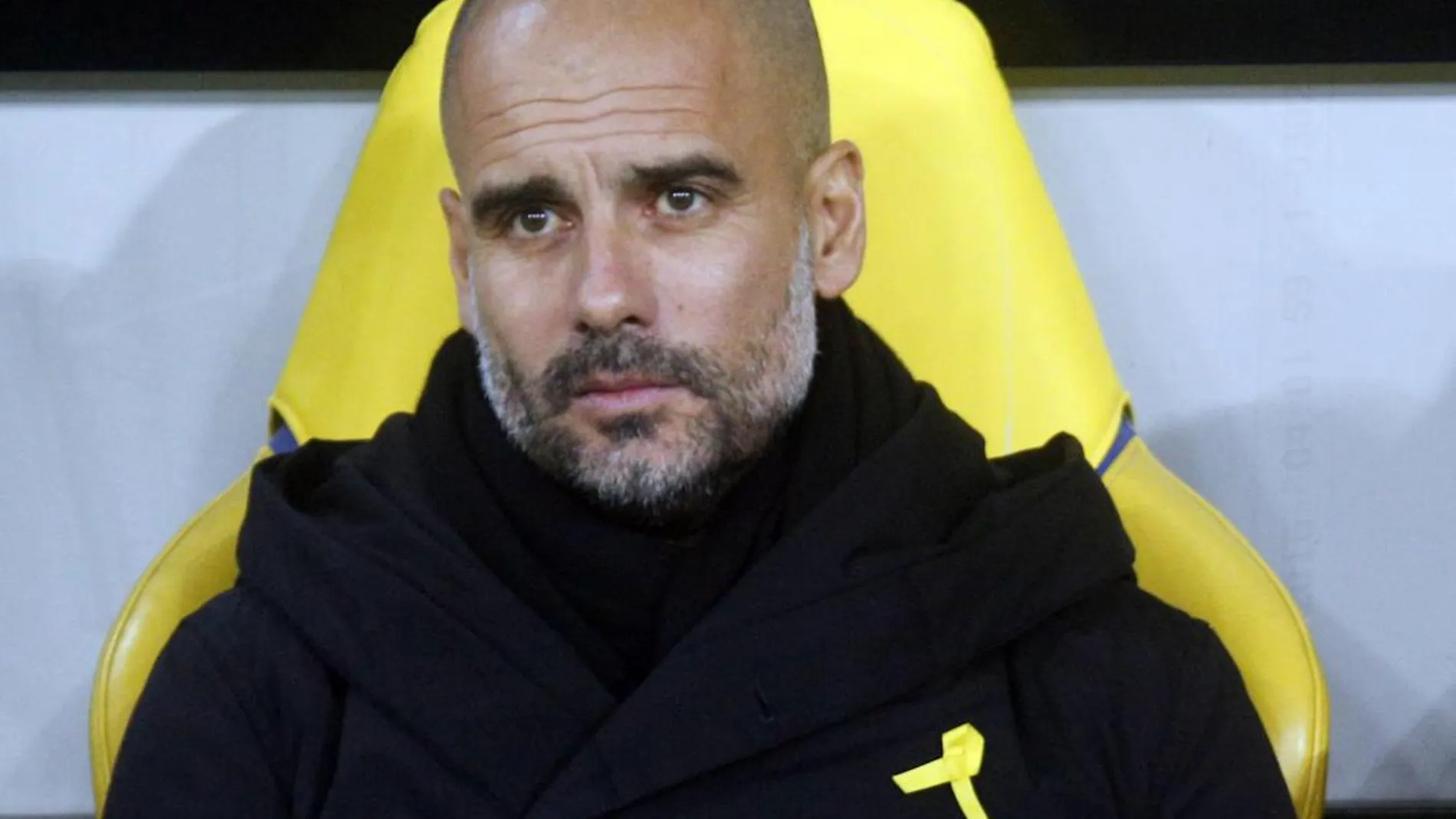 Pep Guardiola en el banquillo durante un partido de Champions League con el lazo amarillo visible sobre su pecho.