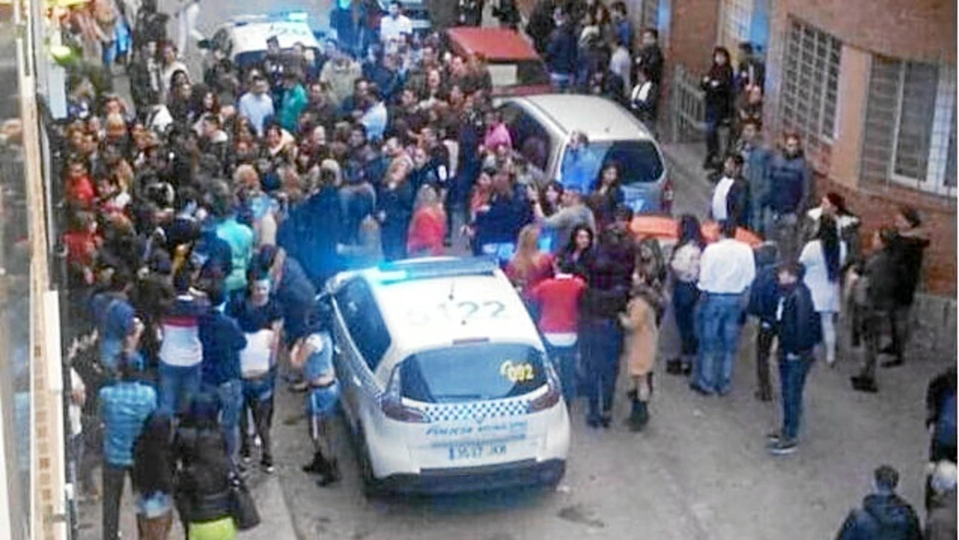 La gente rodea a un coche patrulla durante la redada en un bar de la calle san Enrique de Tetuán