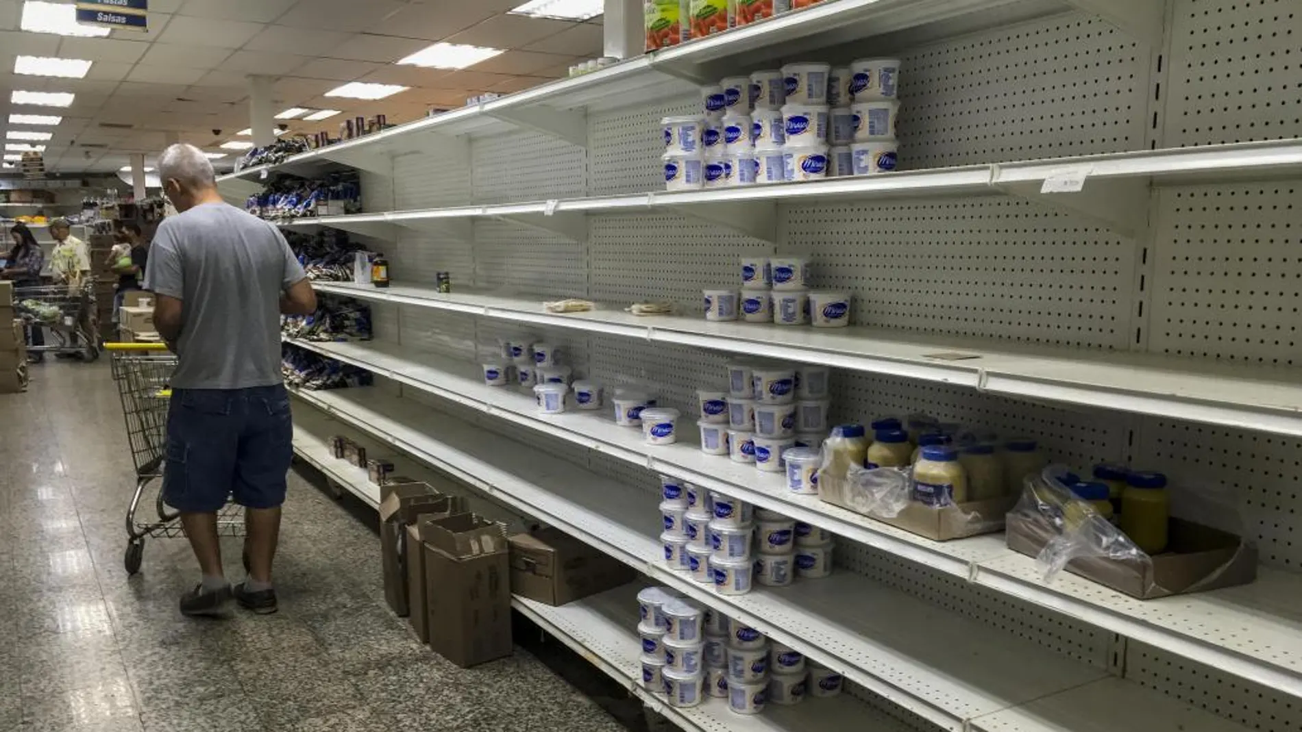 Los clientes buscan alimentos en un supermercado con las estanterías parcialmente vacías en Caracas (Venezuela).