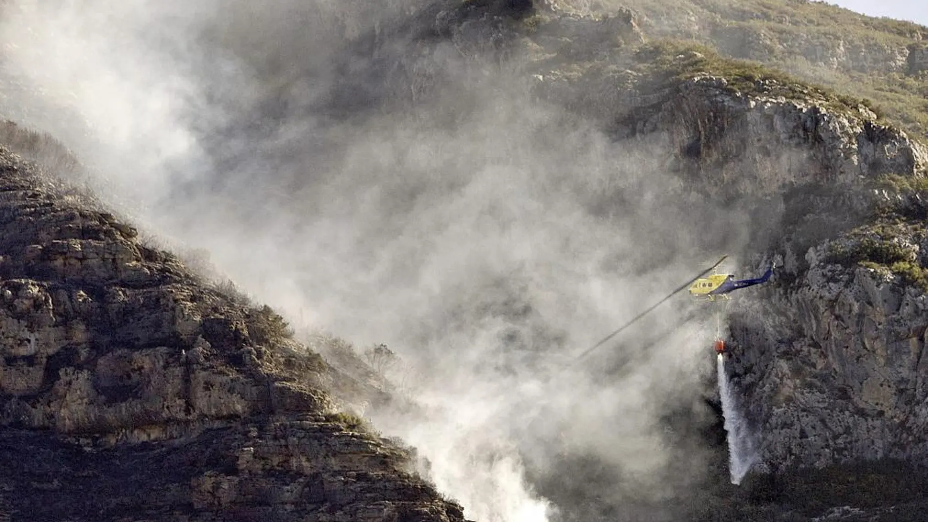Un helicóptero arroja agua en el frente del incendio forestal que afectó el año pasado a los municipios de Barx, Simat y Xeresa